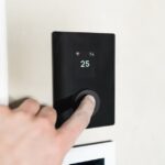Close-up of a hand adjusting a sleek, modern smart thermostat on a wall.